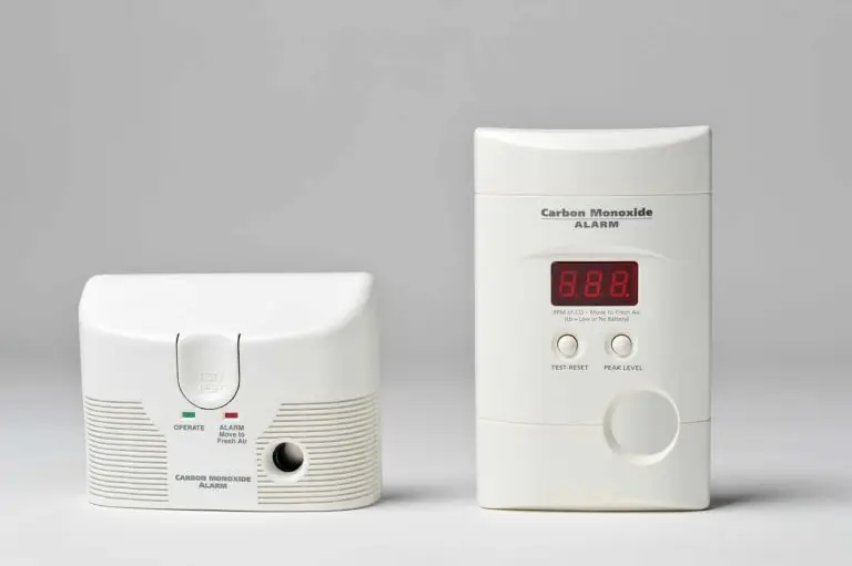 Two types of carbon monoxide alarms on a plain background, one with a digital display and another with a test button and led indicators.