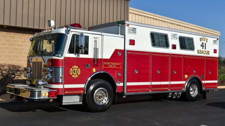 Red and white fire rescue truck with "Dive 41 Rescue" on the side, parked outside a beige industrial building, on a sunny day.