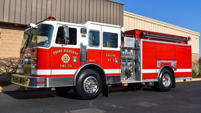 A red and white fire truck labeled "Point Pleasant Fire Co. Engine 41-2" is parked outdoors on a sunny day. The truck features shiny chrome details and various equipment compartments on its side.